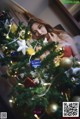 A woman in a red dress sitting next to a Christmas tree.